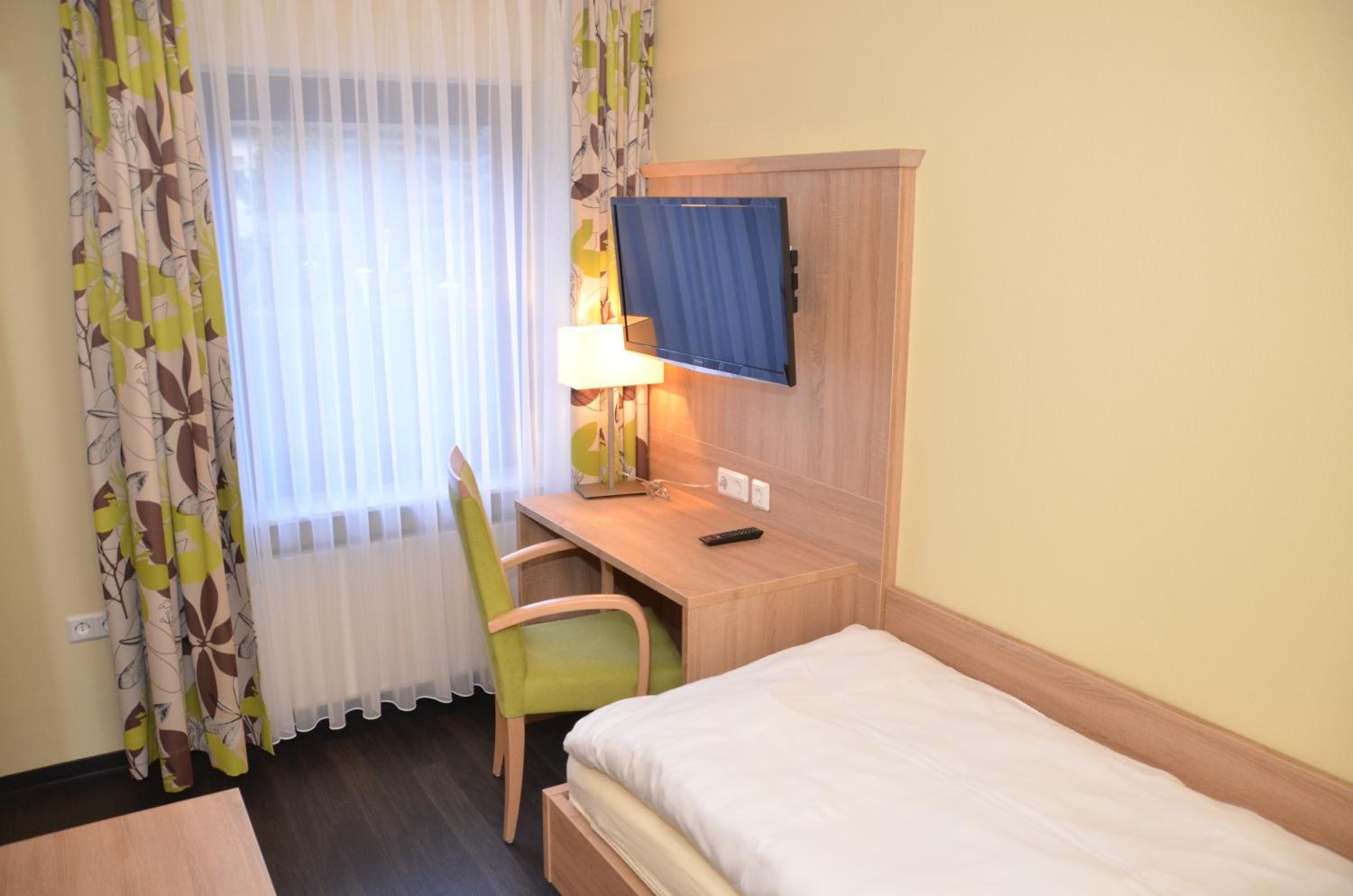 A hotel room with a bed, a desk with a chair, a television, and a window with curtains.