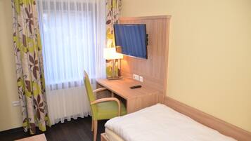 A hotel room with a bed, a desk with a chair, a television, and a window with curtains.