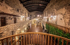 A stone-walled corridor with wooden railings, a wooden staircase, and a central open area with tables and chairs. - Castello di Limatola (Limatola)