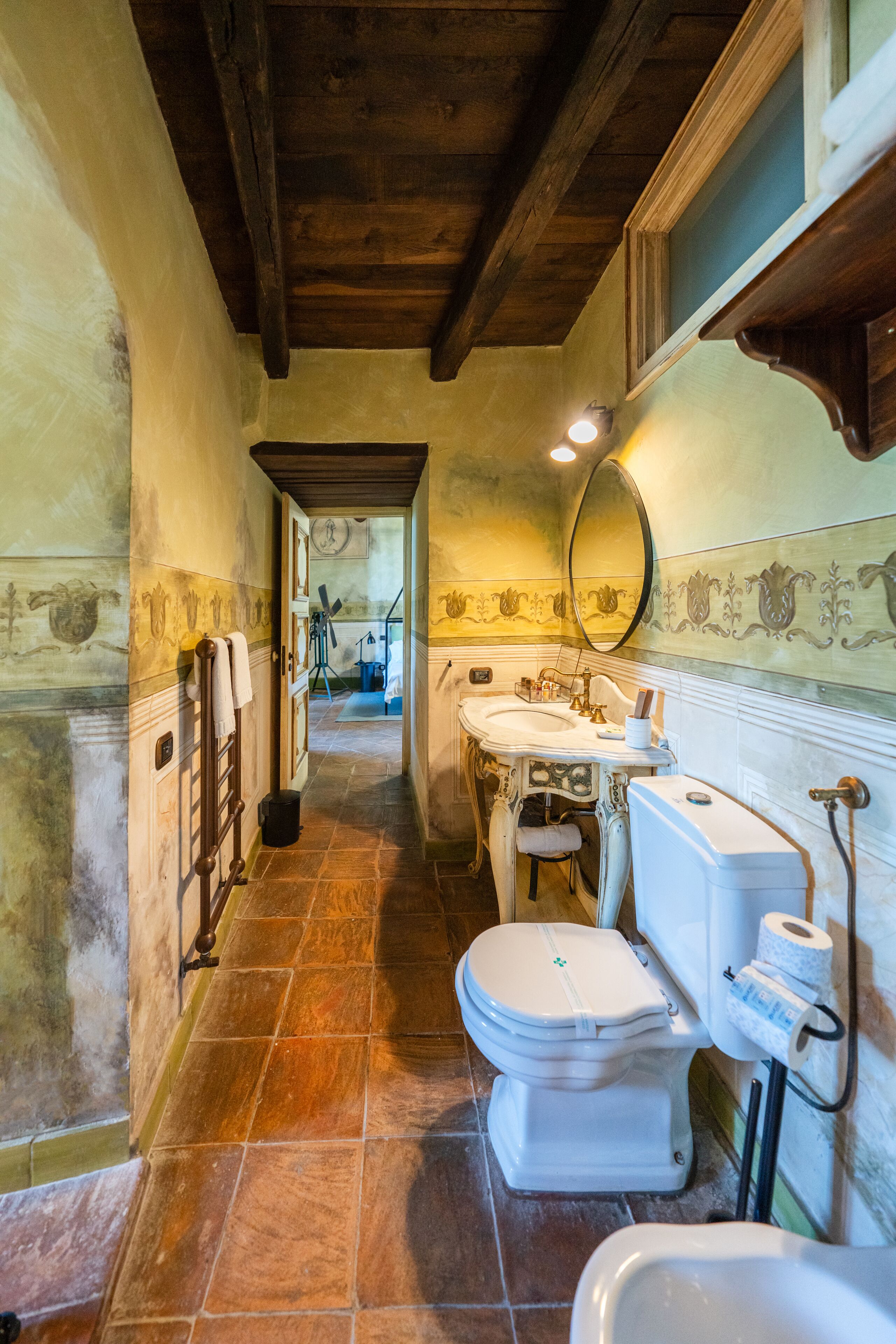 Un pasillo estrecho con un baño a la derecha, que incluye inodoro, lavabo y espejo.