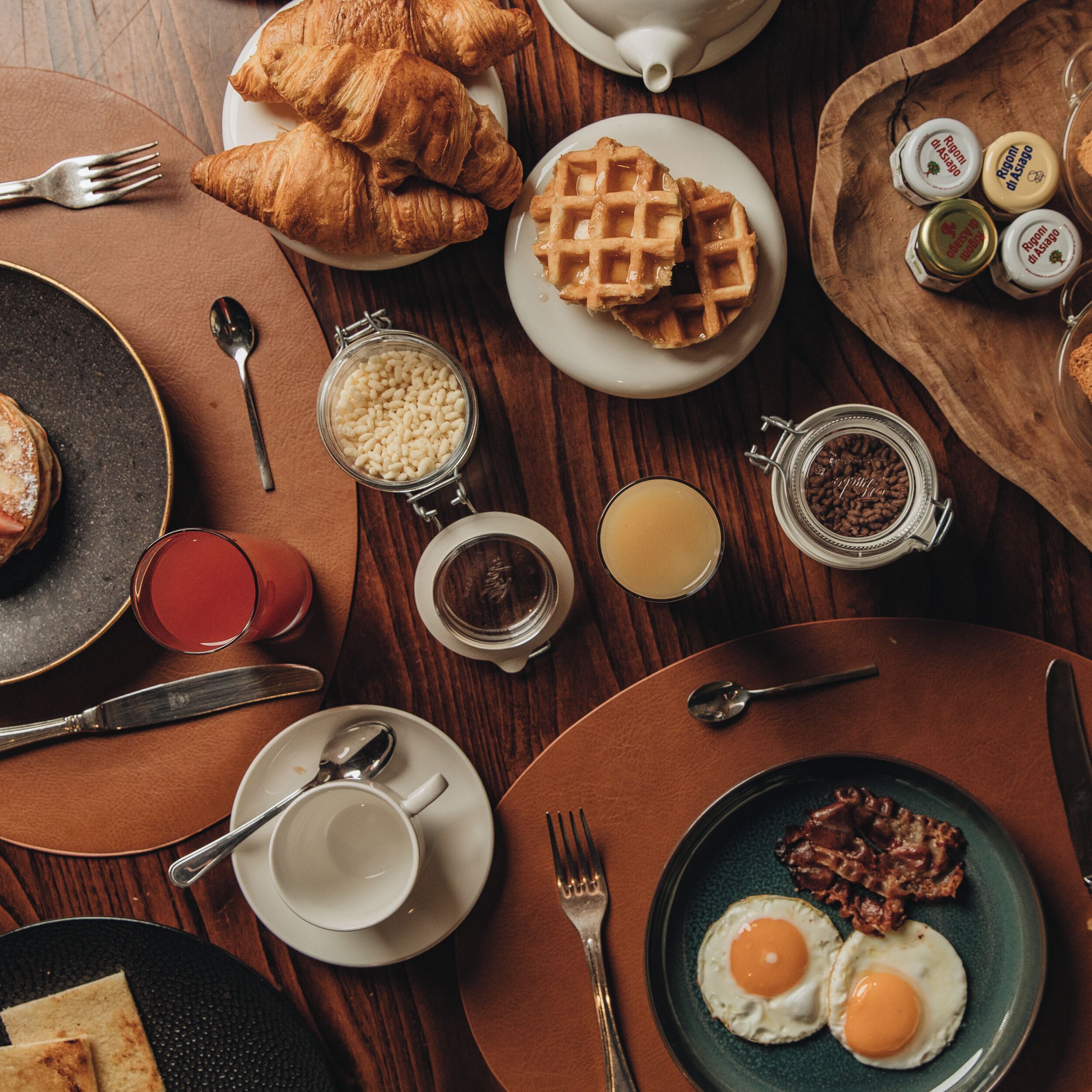 A breakfast setting with croissants, waffles, eggs, and various condiments on a wooden table.