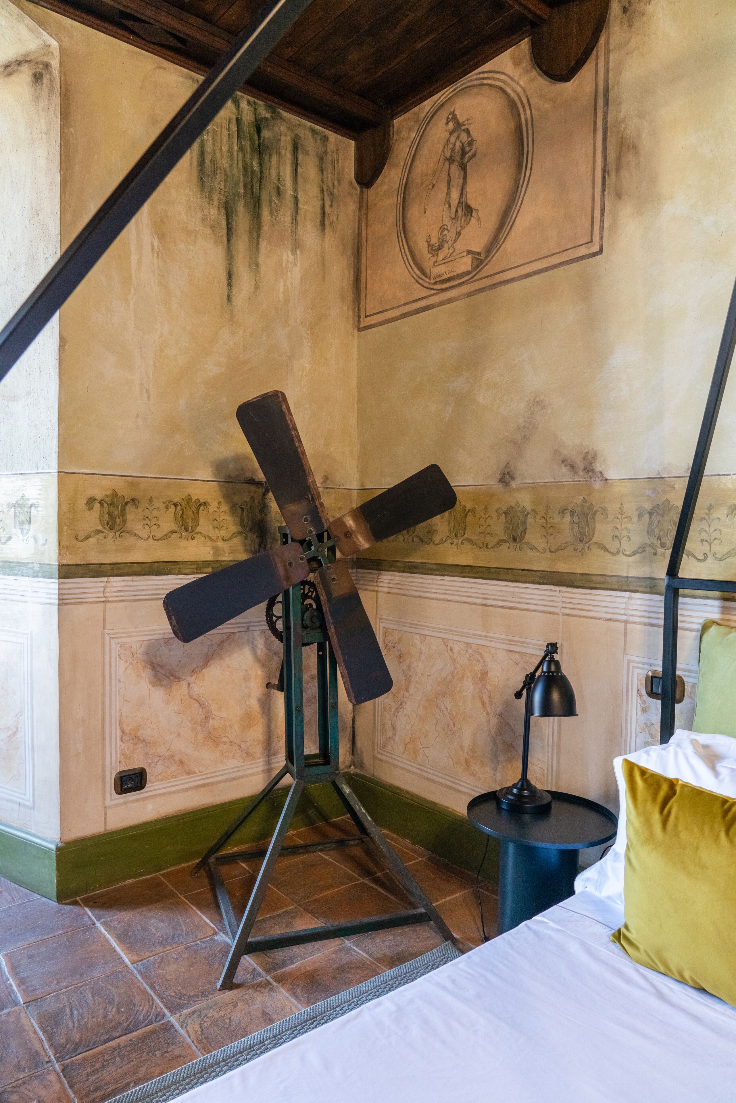 Ein Zimmer mit einem Bett, einem Standventilator, einer Lampe und einer Wand mit einer Zierverkleidung.