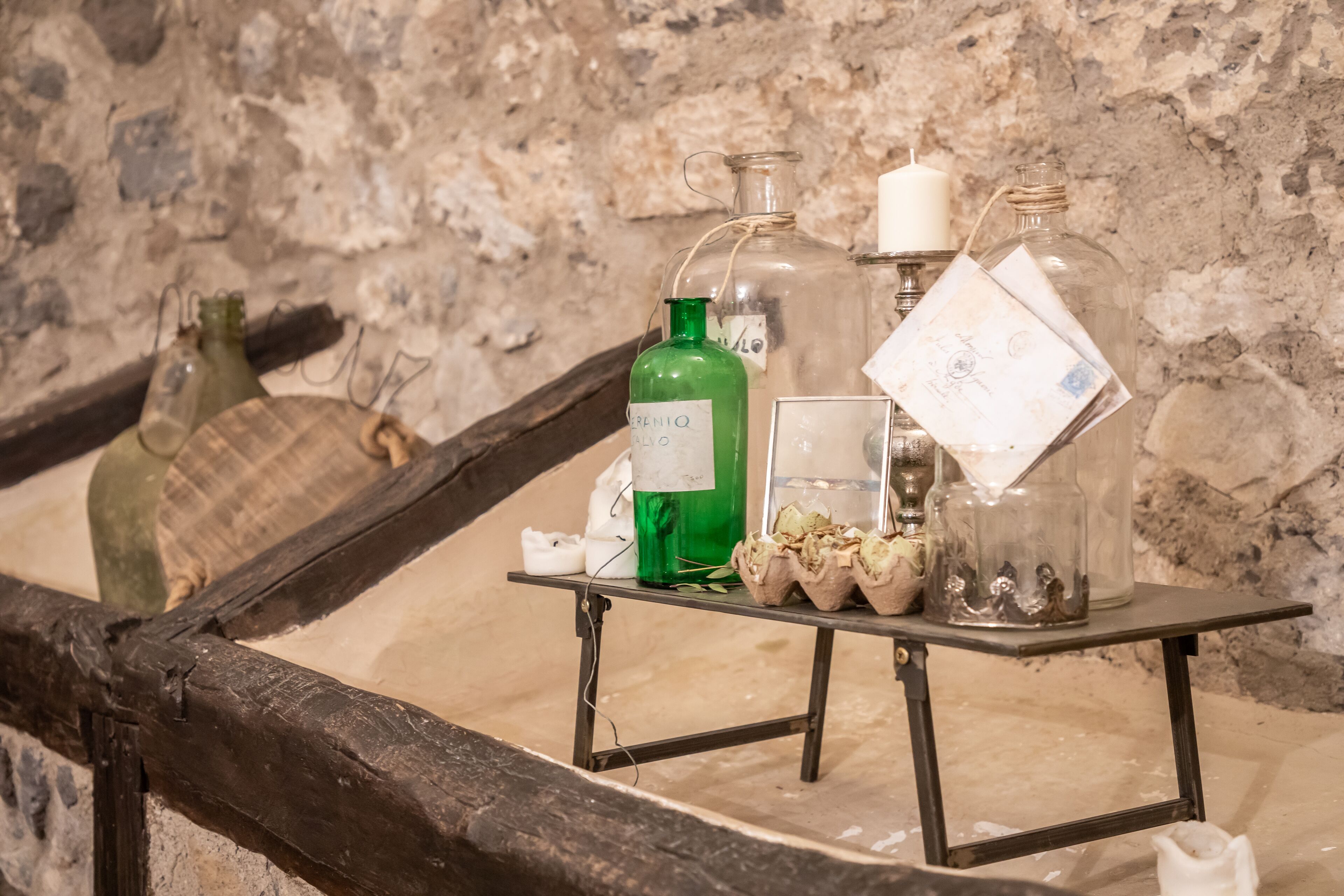 Une table sur laquelle sont disposées différentes bouteilles en verre et une bougie, le tout placé devant un mur de pierre.