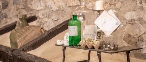 Una mesa con varias botellas de vidrio y una vela, frente a un muro de piedra.