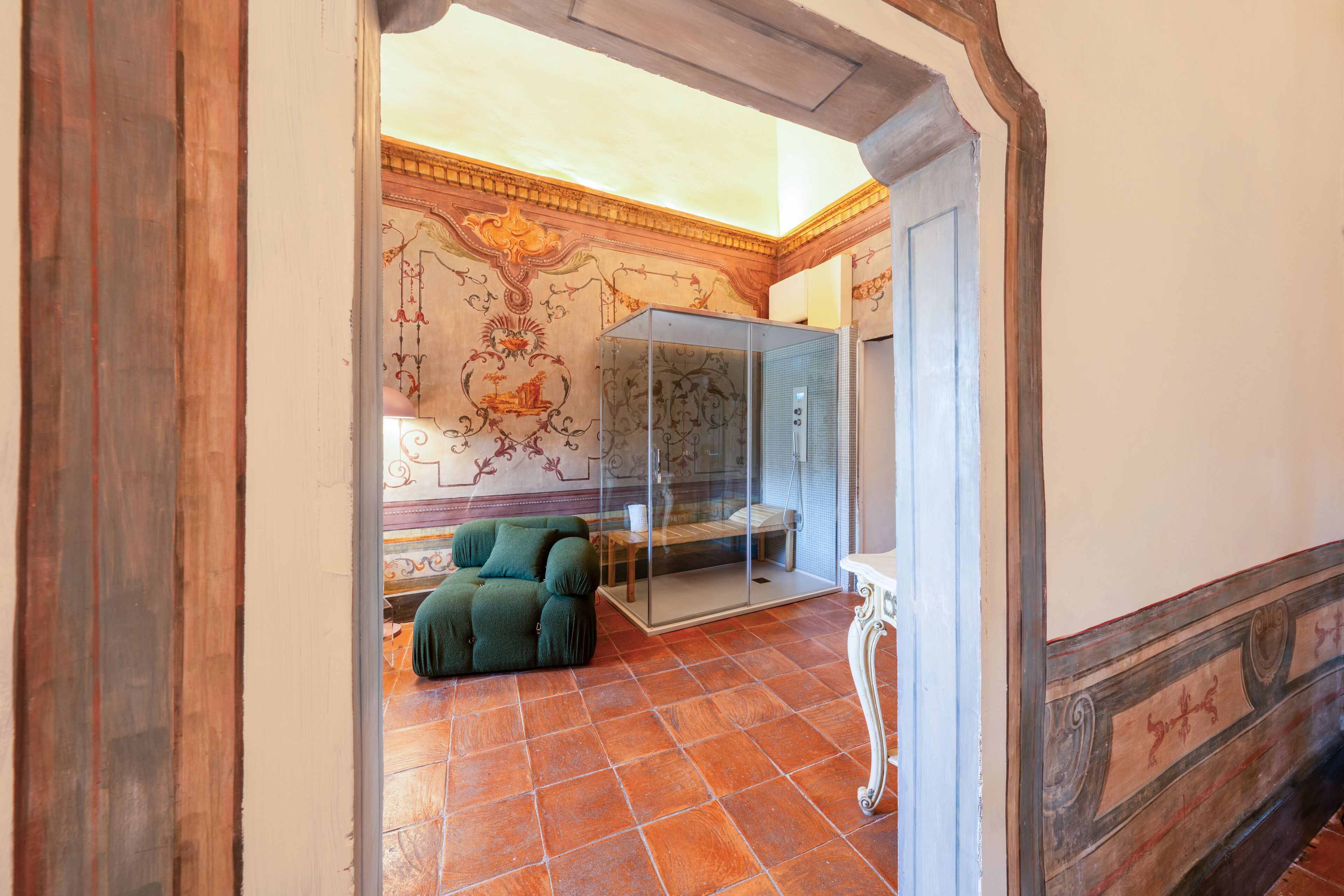 A room with a green sofa, a glass-enclosed area, ornate wall decorations, and a tiled floor.
