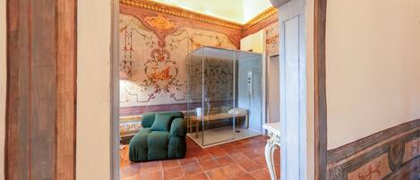 A room with a green sofa, a glass-enclosed area, ornate wall decorations, and a tiled floor.