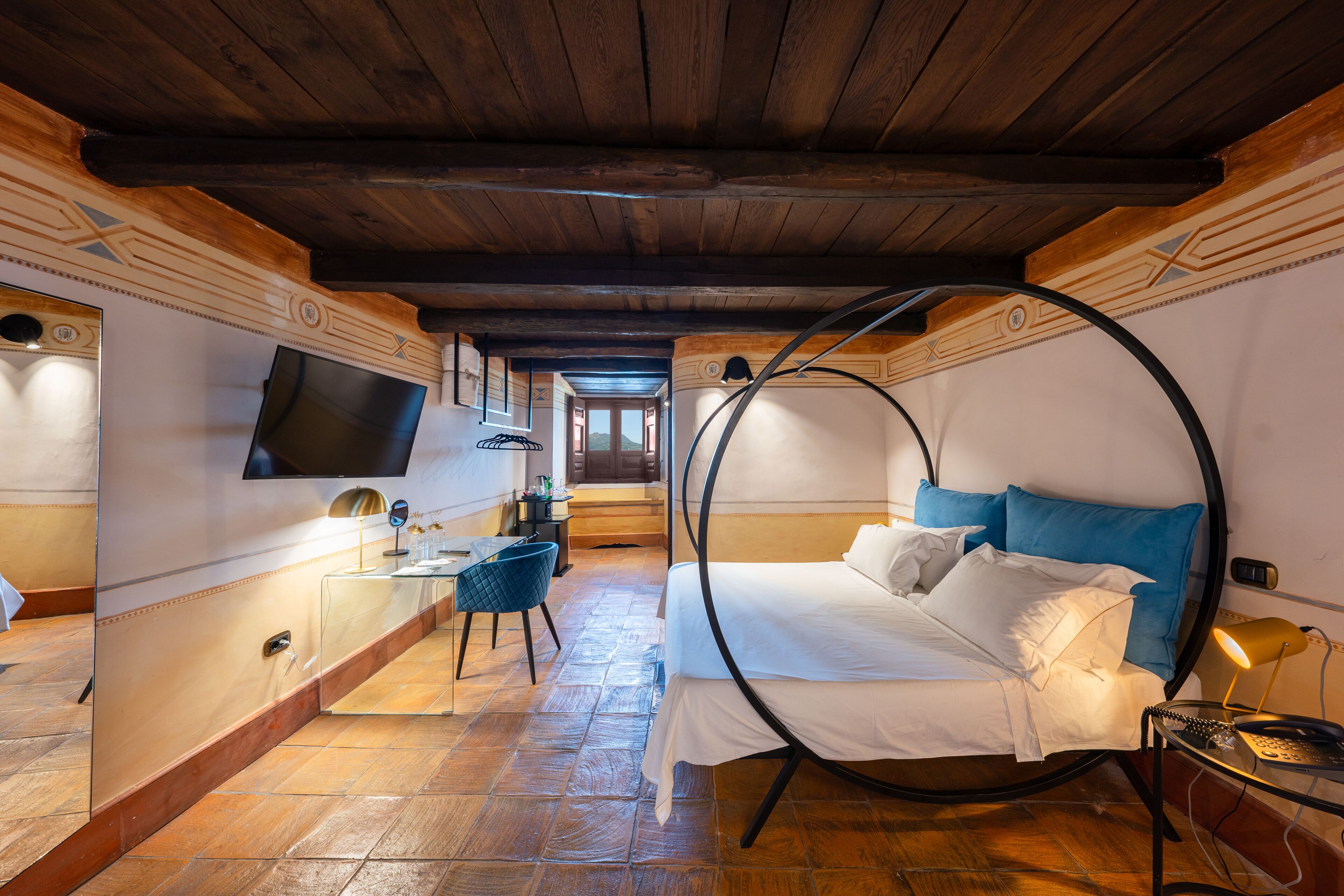 A bedroom with a circular bed, a desk, a chair, a TV, and a mirror.