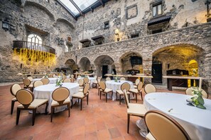 Un amplio patio con muros de piedra, varias mesas redondas con sillas y una fuente central.