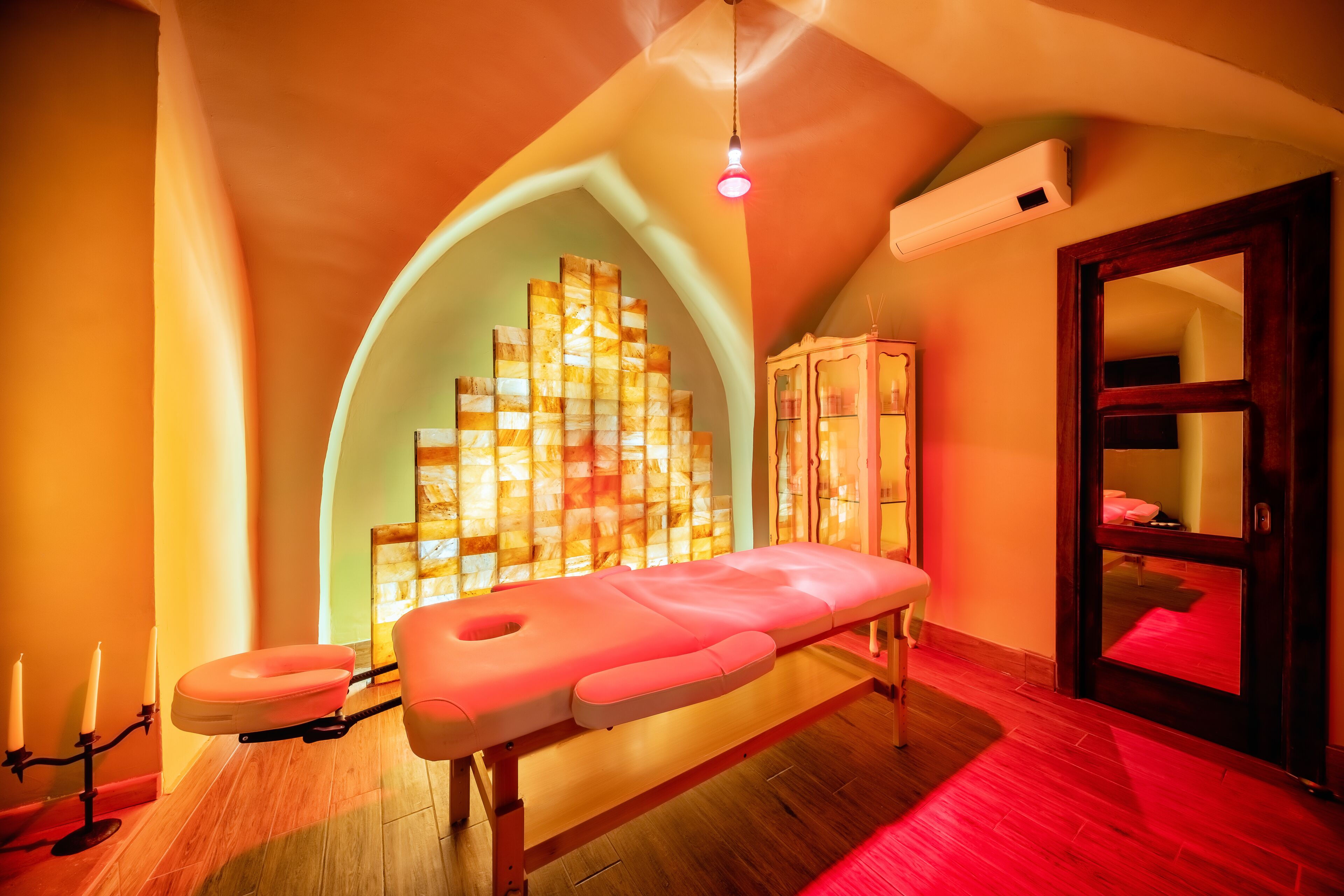 A room with a wooden floor, a massage table, a cabinet, and a mirror.