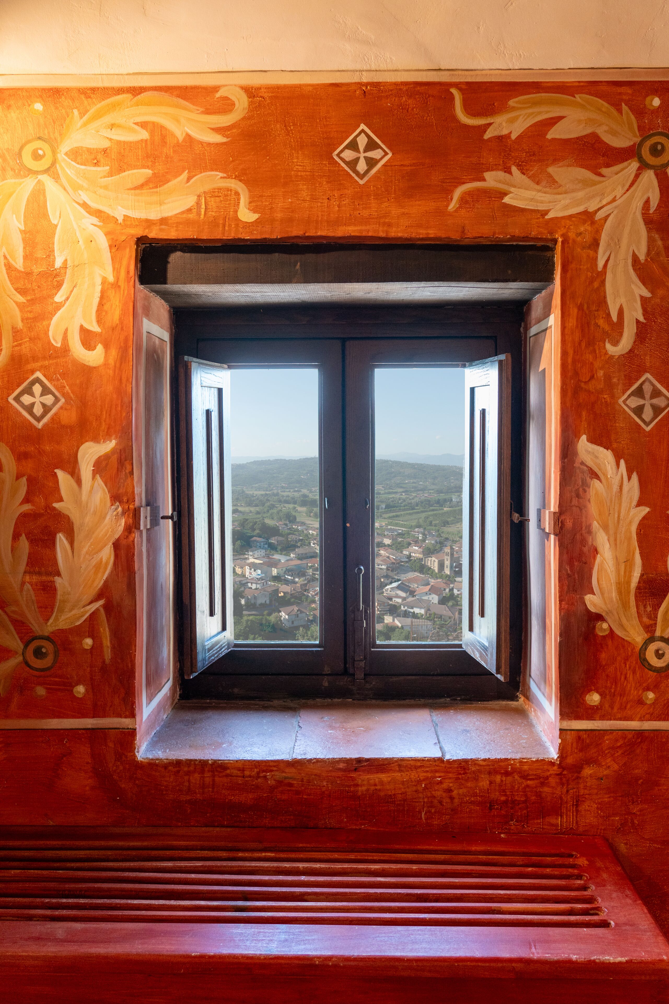 A wooden door with a window, flanked by ornate wall designs, leading to a view of a town.