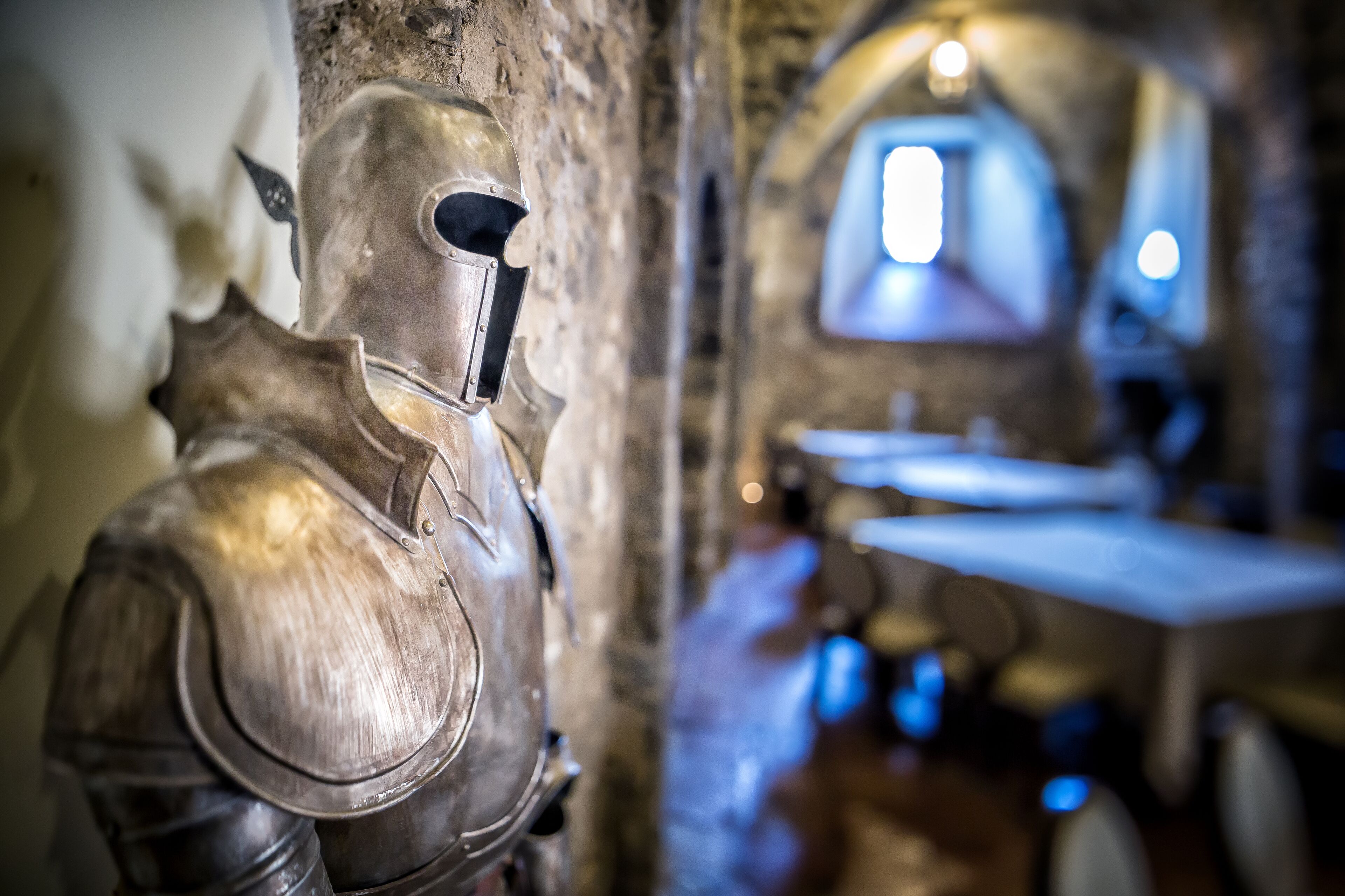 Une armure de chevalier médiéval dans une pièce faiblement éclairée, aux murs de pierre et dotée d’une fenêtre.