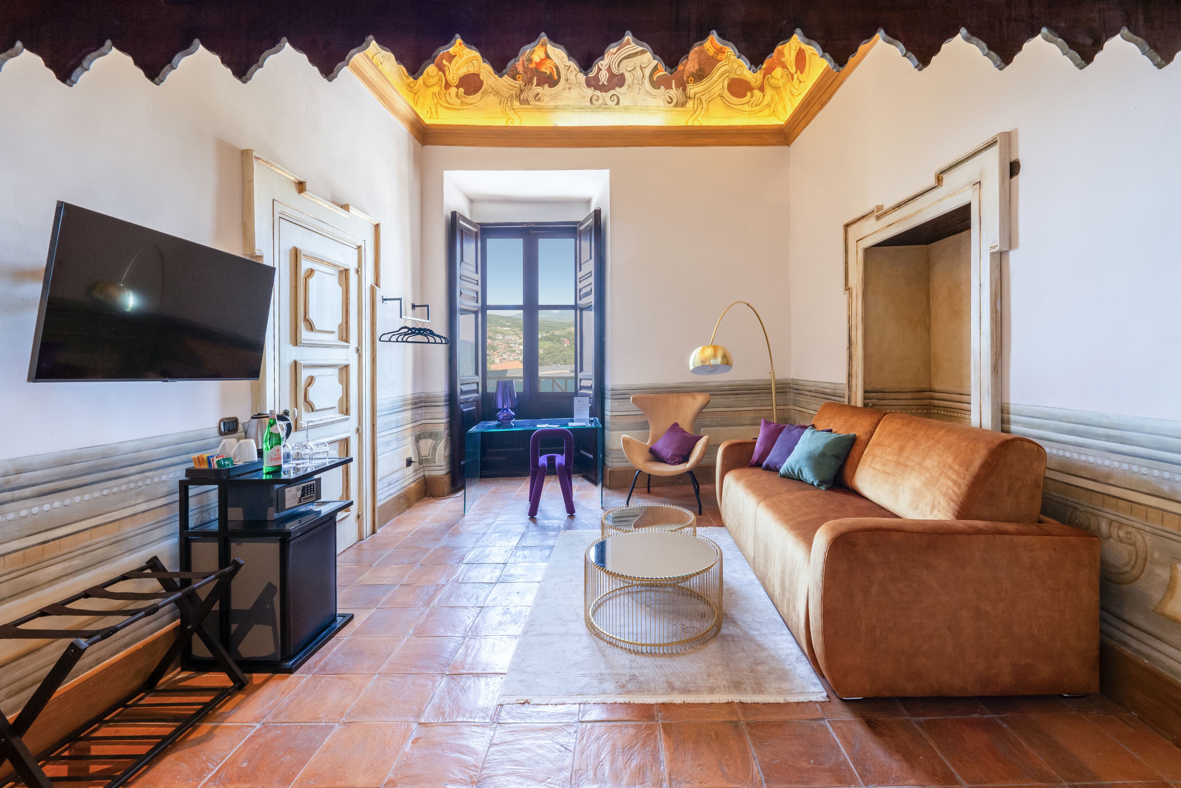 Una sala de estar con sofá, televisión, escritorio con lámpara y vista a través de una puerta abierta.