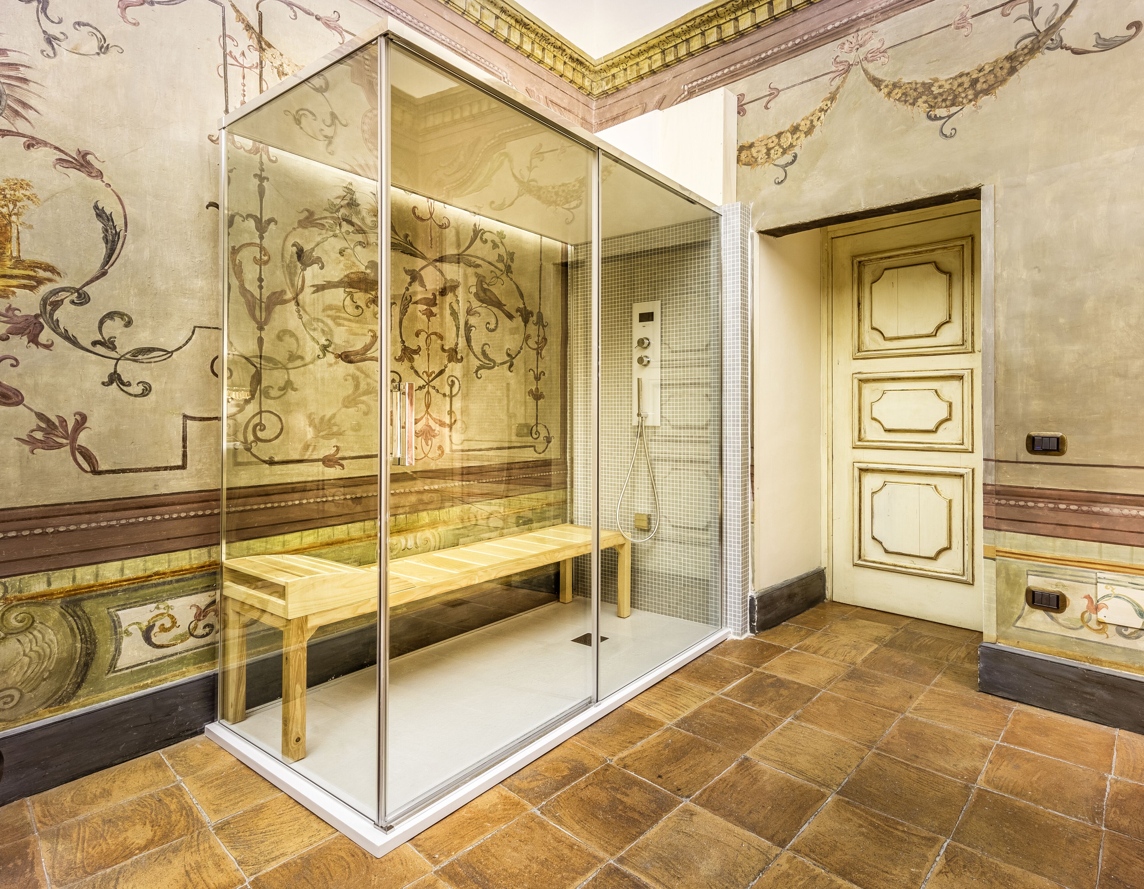 A room with a glass partition, a bench, ornate wall designs, and a tiled floor.