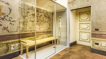 Una habitación con separador de vidrio, un banco, diseños ornamentales en la pared y suelo de baldosas.