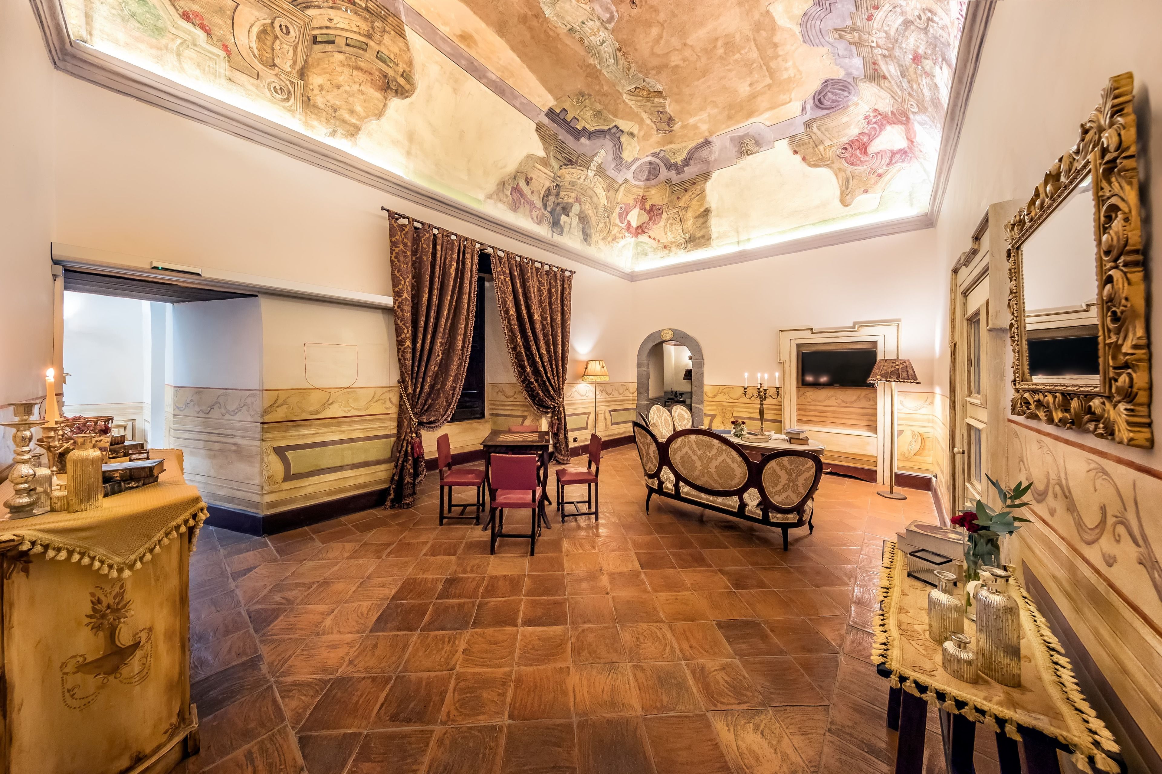 Un lobby de hotel lujoso con techo alto, elaborados adornos en el techo, un mostrador de recepción de mármol, un área de descanso con sillas y una mesa decorativa con jarrones.