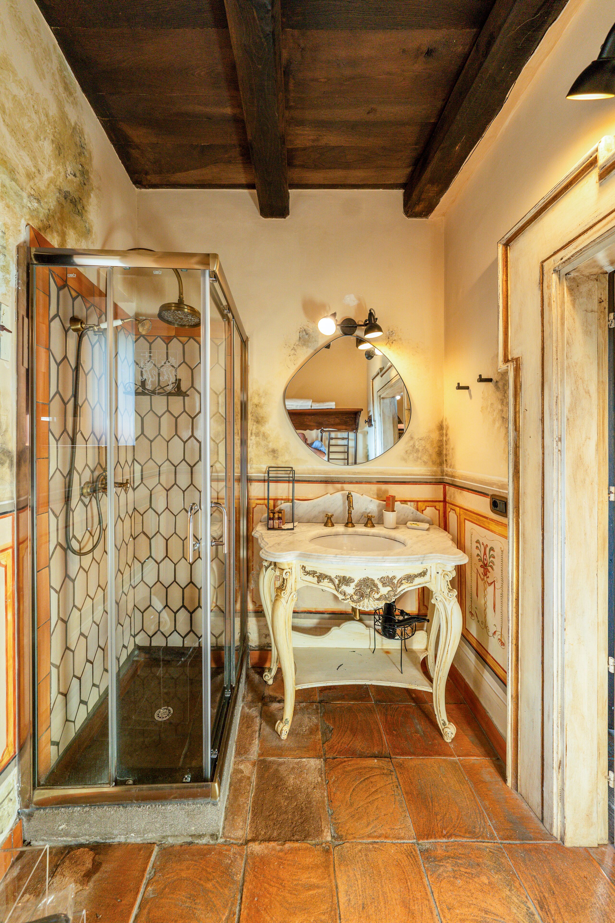 Un baño con ducha de vidrio, un lavabo con detalles ornamentales y un espejo sobre él.