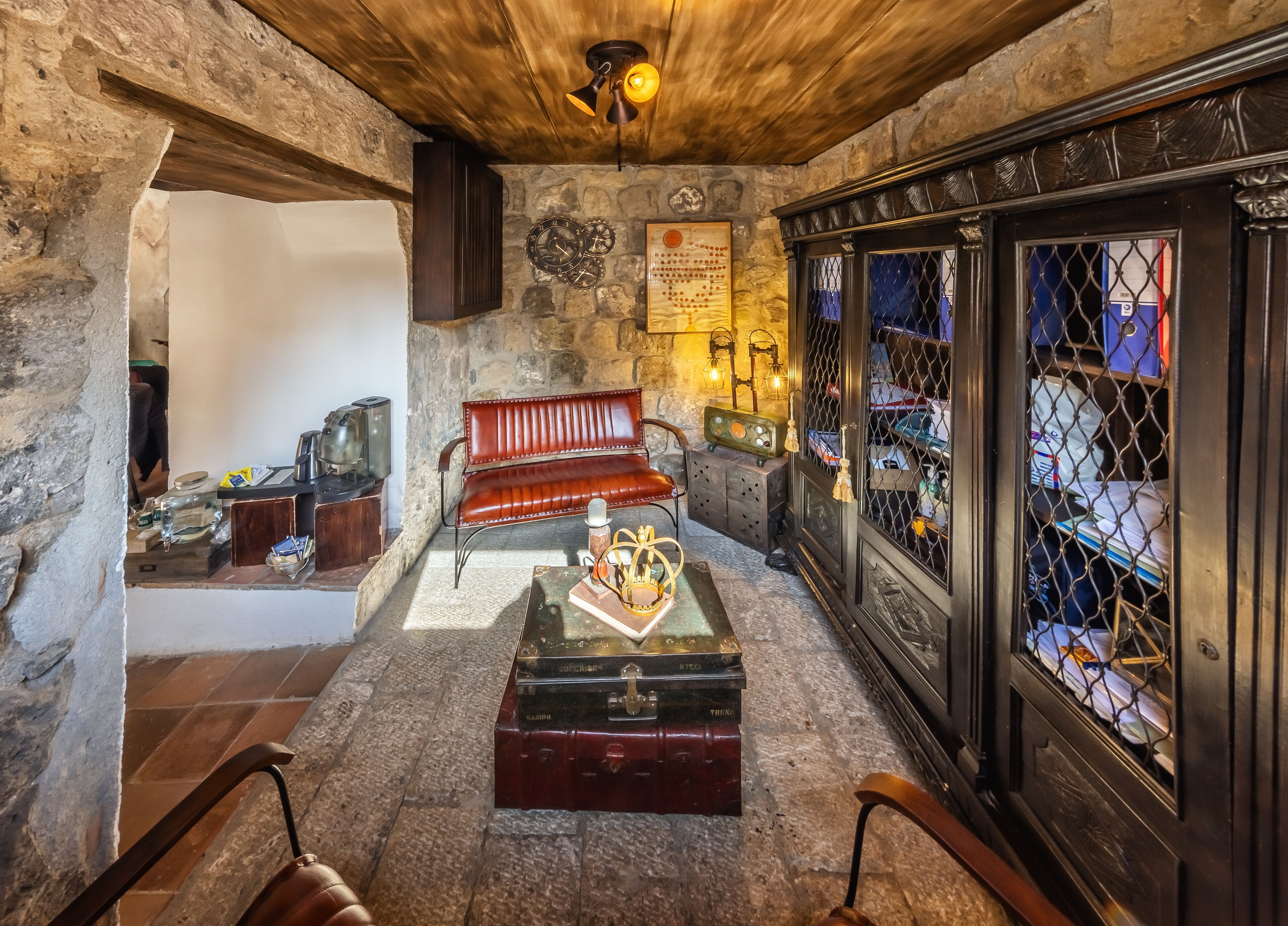 A cozy room with a stone wall, a wooden ceiling, a red leather bench, a vintage radio, and a metal gate with a view of the outside.
