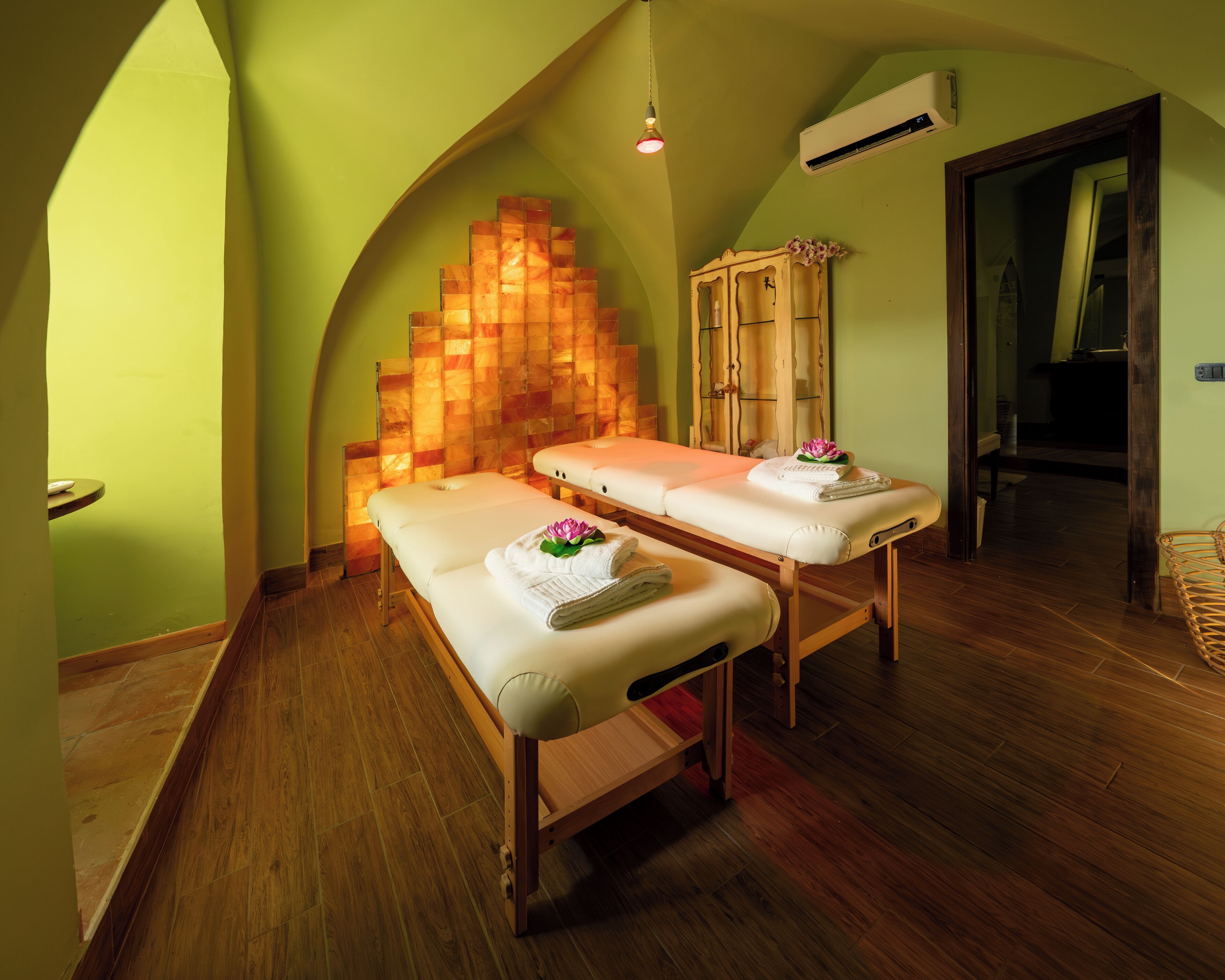 Un cuarto de spa con dos camillas de masaje, un armario de madera y un aire acondicionado instalado en la pared.