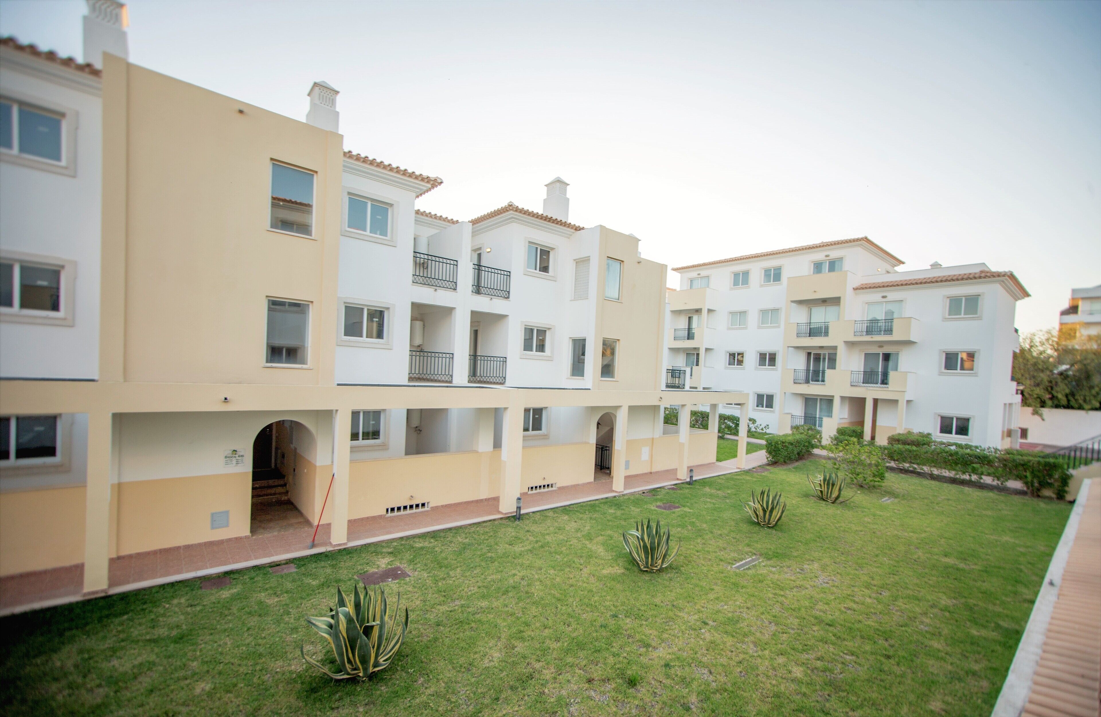 Un edificio residencial de varios pisos con balcones, un patio central y un césped bien cuidado.