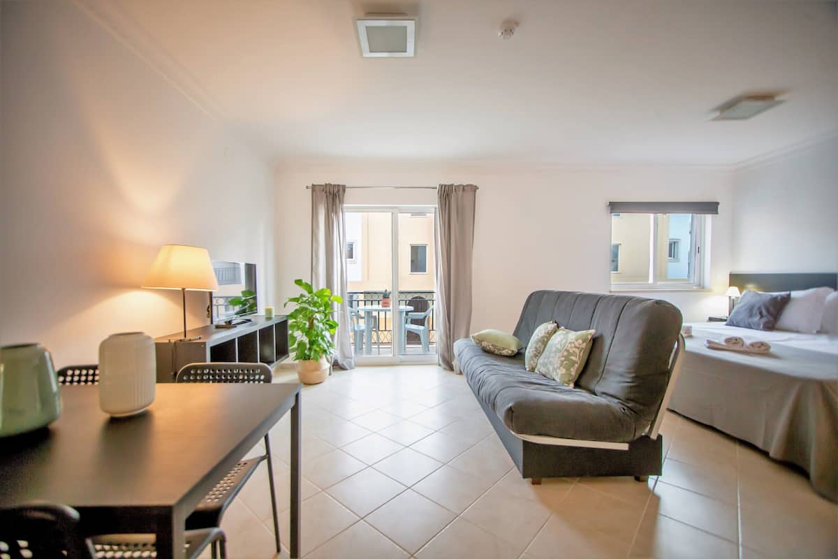 Une chambre d’hôtel moderne dotée d’un canapé, d’un lit, d’un coin repas avec une table et des chaises, et d’un balcon offrant une vue agréable.