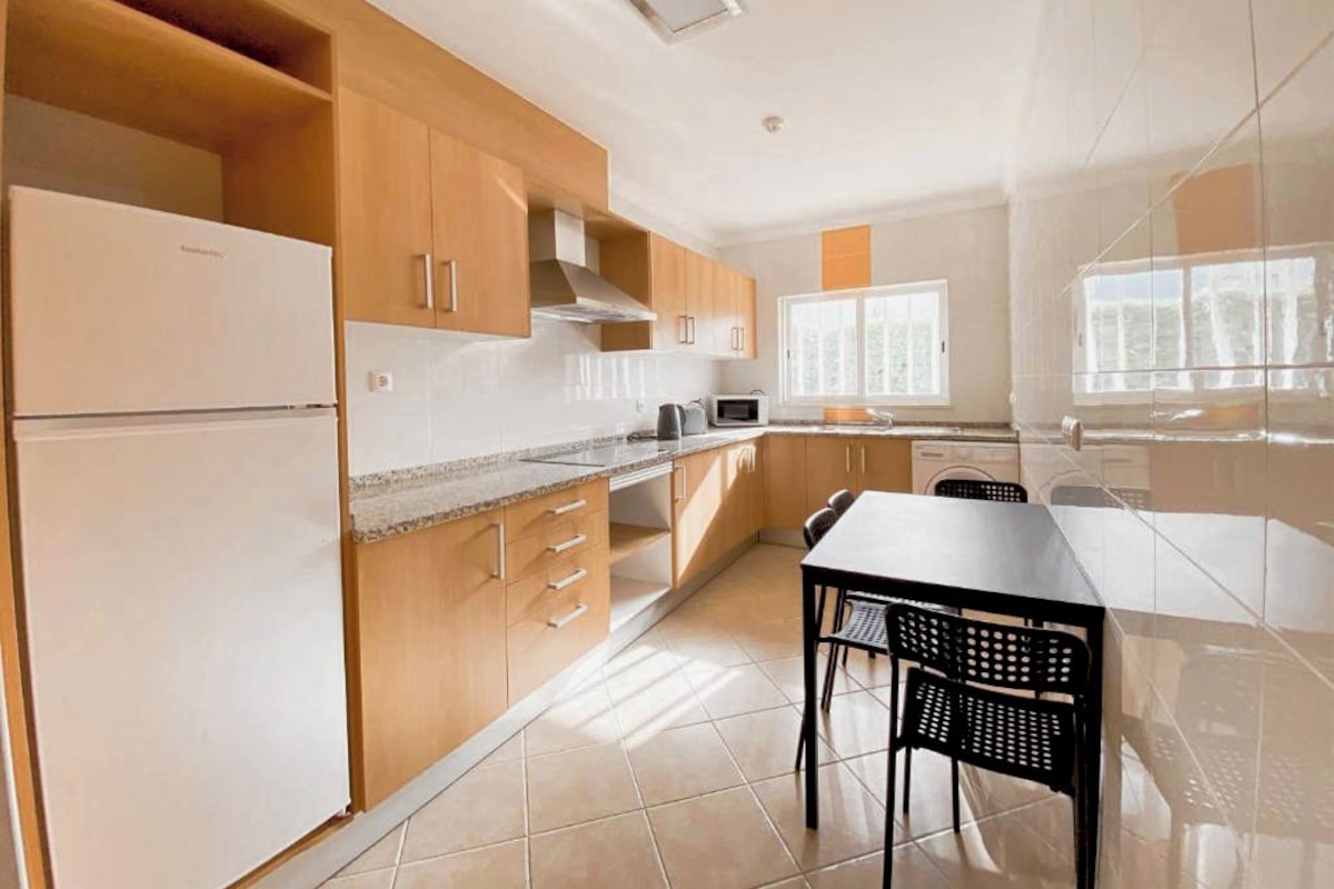 A modern kitchen with wooden cabinets, a built-in microwave, and a dining area with a table and chairs.