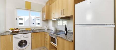 A modern kitchen with wooden cabinets, a built-in washing machine, a microwave, and a refrigerator.