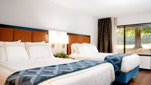 Ein Hotelzimmer mit zwei Betten, einem großen Fenster mit Blick auf Bäume und einem Holzboden.