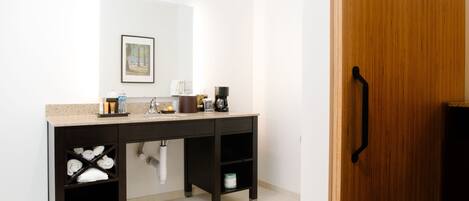 Un baño moderno con un mueble de tocador de madera oscura, un lavabo y un espejo. Hay toallas y artículos de aseo en el mueble, y se ve un inodoro debajo del lavabo.
