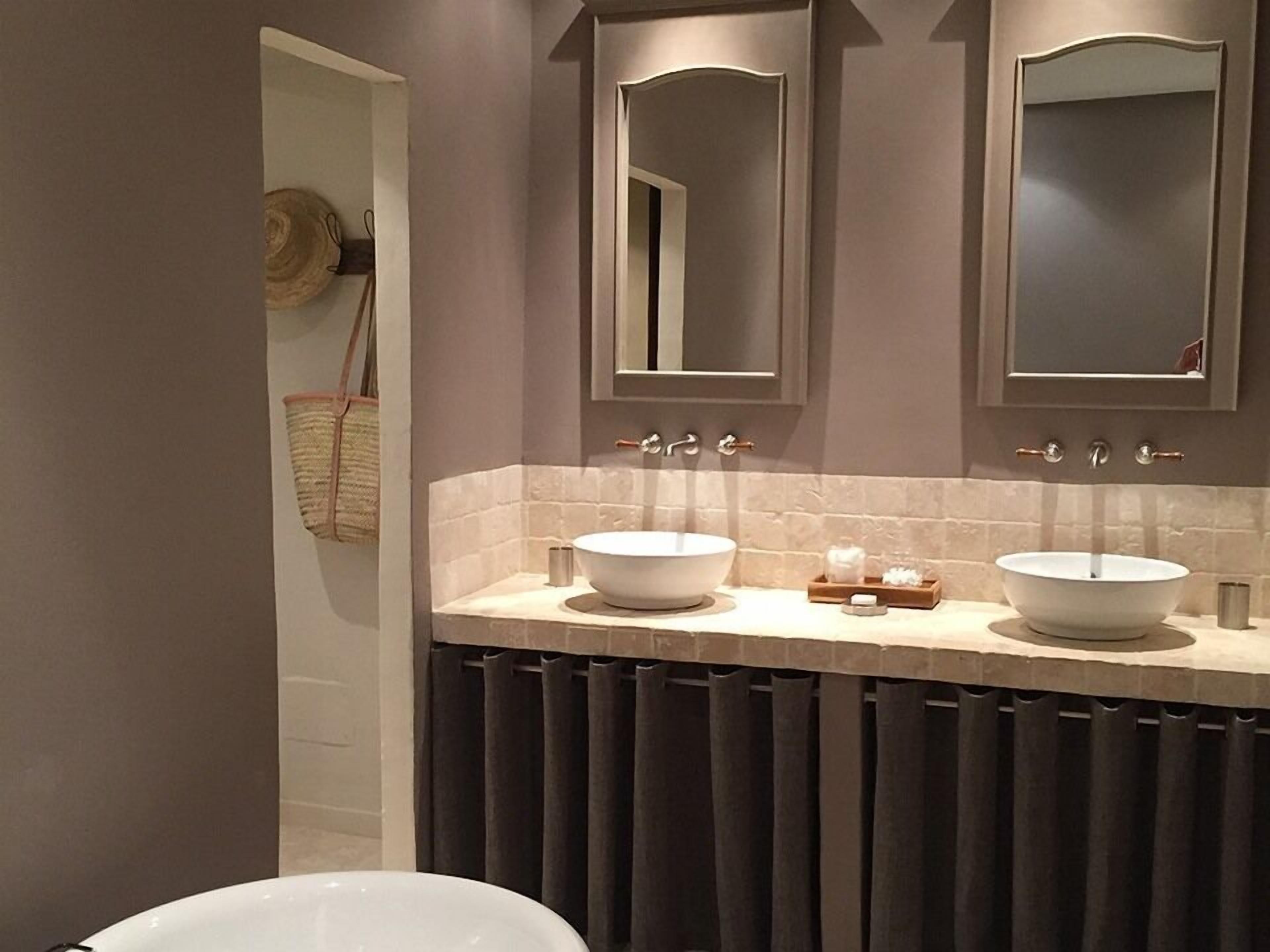 A bathroom with two large white sinks, a mirror above each sink, and a towel rack with a woven bag.