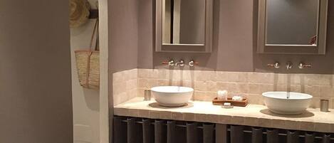 A bathroom with two large white sinks, a mirror above each sink, and a towel rack with a woven bag.