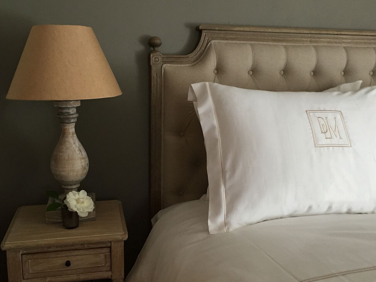 A bed with a tufted headboard, a bedside table with a lamp, and a pillow with initials.