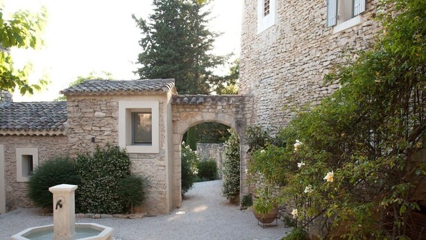 A courtyard with a stone fountain, a small archway, and a building with a tiled roof.