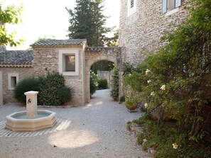 Une cour avec une fontaine en pierre, une petite arche et un bâtiment doté d’un toit en tuiles.