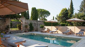 A pool area with lounge chairs and umbrellas, surrounded by stone walls and greenery.