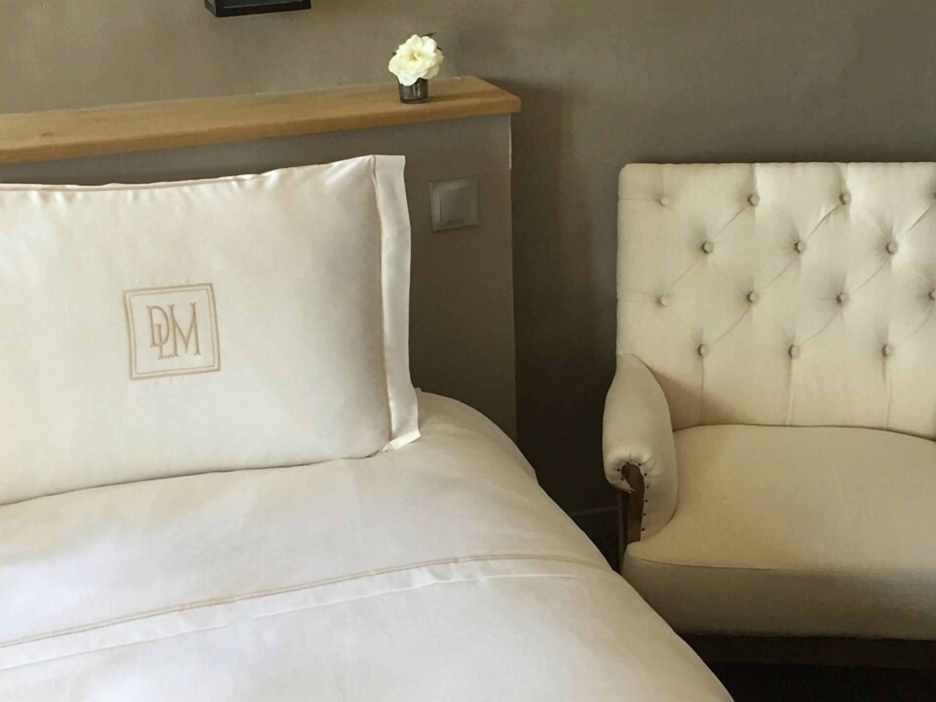 A bed with a pillow marked "DM" and a tufted armchair.