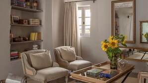 A living room with two armchairs, a coffee table with books and a vase of sunflowers, a bookshelf with books and decorative items, and a large mirror on the wall.