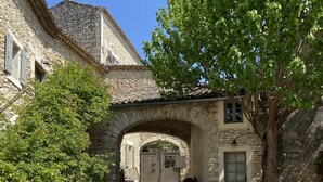 A stone building with an arched entrance, a gravel courtyard, and a water fountain.