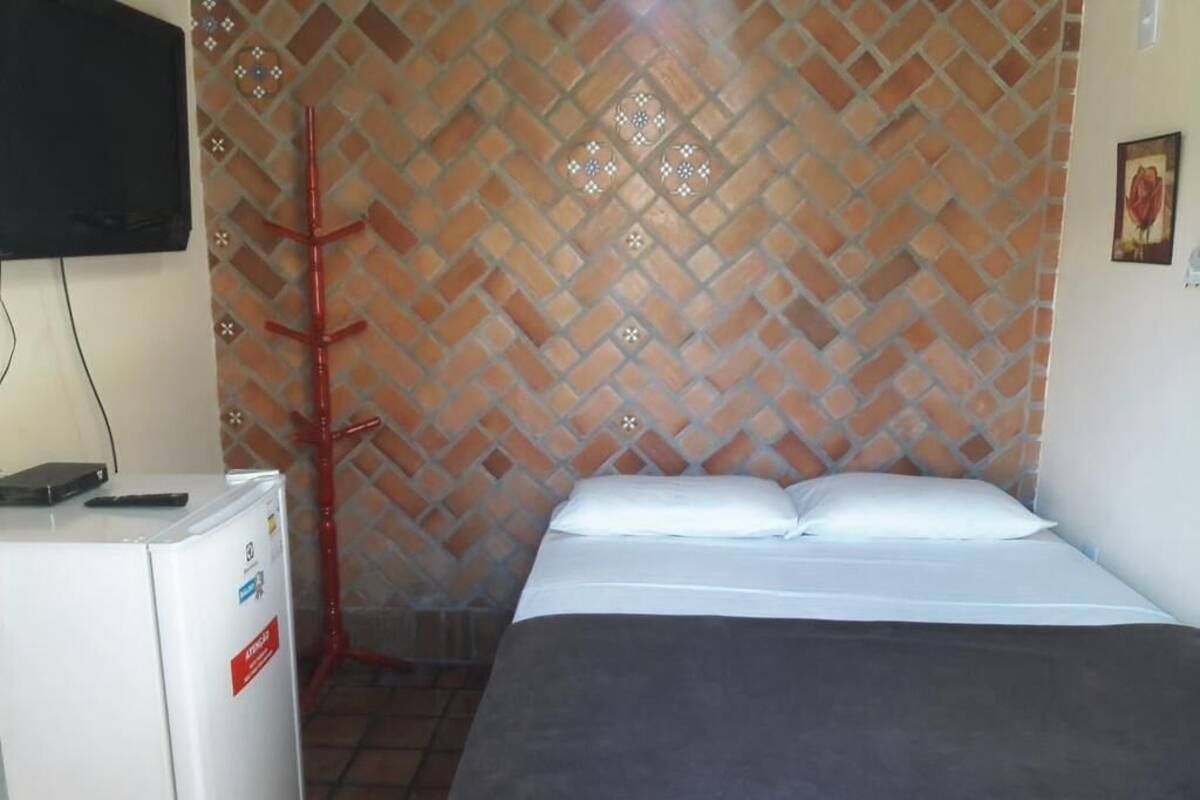 A room with a bed, a white refrigerator, a TV mounted on the wall, and a patterned wall.
