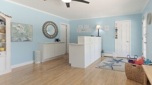 Ein Zimmer mit hellblauen Wänden, Holzboden, Deckenventilator, einem Teppich mit Seesternen und einer weißen Tür.