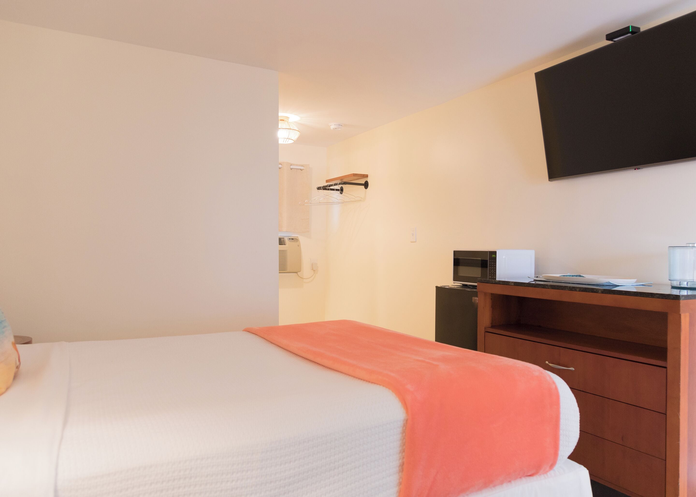 A hotel room with a bed, a desk with a microwave, and a flat-screen TV mounted on the wall.