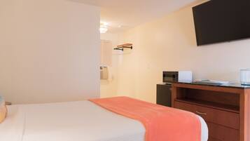 A hotel room with a bed, a desk with a microwave, and a flat-screen TV mounted on the wall.
