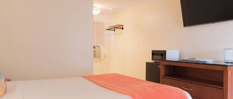 A hotel room with a bed, a desk with a microwave, and a flat-screen TV mounted on the wall.