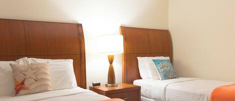 A hotel room with two beds, each with a wooden headboard, a bedside table with a lamp, and a nightstand with a power outlet.