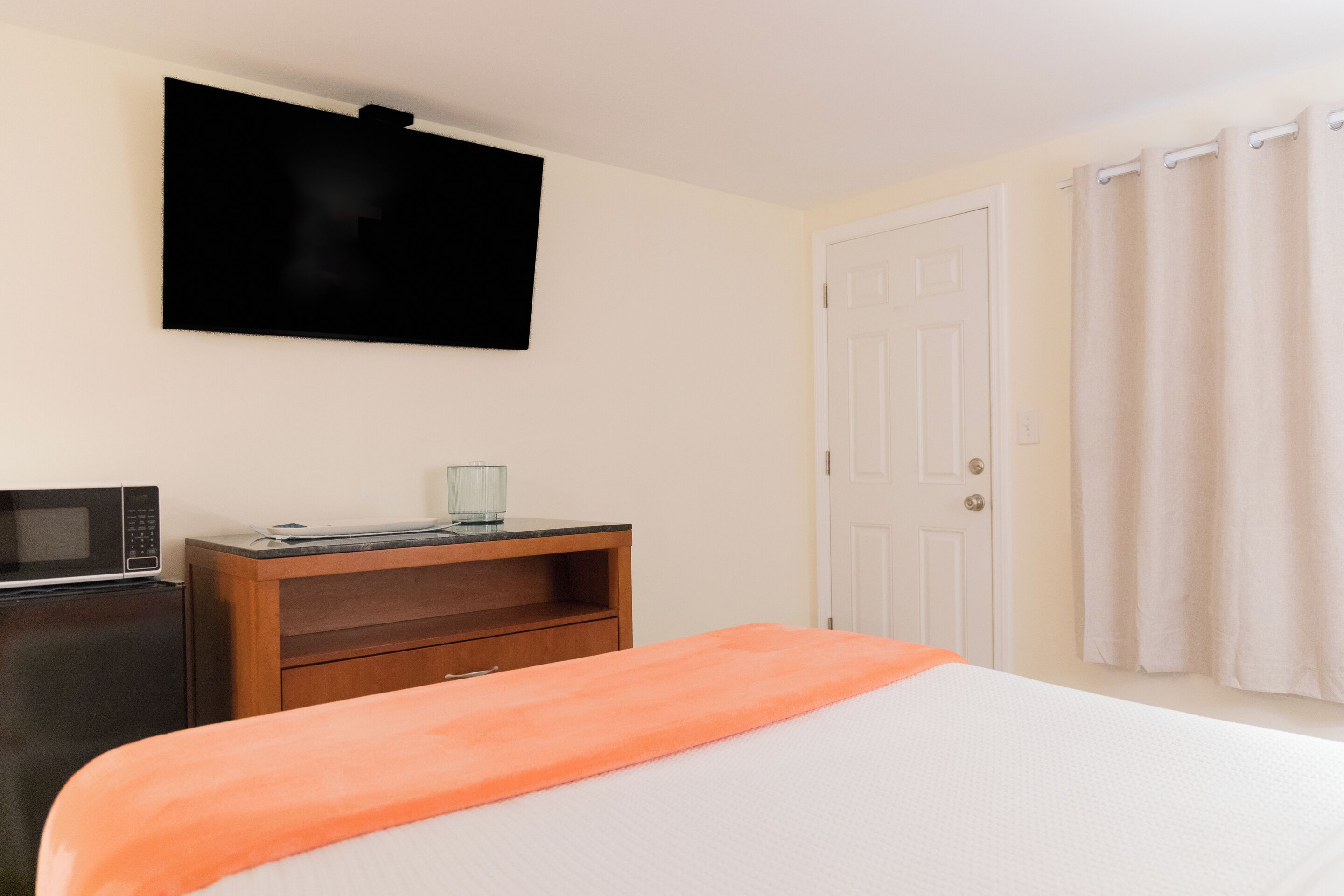 Une chambre d’hôtel équipée d’un lit, d’un téléviseur fixé au mur, d’un four à micro-ondes et d’une commode en bois.