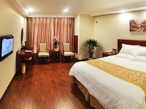 Una camera d'albergo con un letto grande, una scrivania con un computer, due poltrone, una TV, una pianta e un quadro appeso al muro.