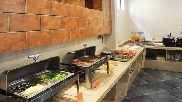 Un buffet proposant différents plats, notamment un bar à salades et des plats chauds, installé dans un espace cuisine moderne avec des murs carrelés et un long comptoir.