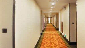 Un long couloir étroit, typique des hôtels, avec un tapis à motifs, des portes des deux côtés et un éclairage au plafond.