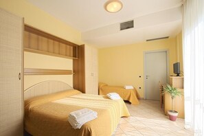 Ein Hotelzimmer mit zwei Betten, einem Kleiderschrank, einem Fernseher und einer Zimmerpflanze.