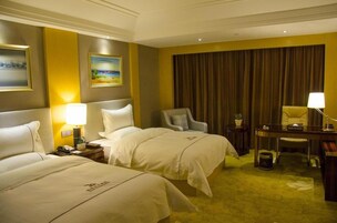 Habitación de hotel con dos camas, un escritorio, una silla, una lámpara y un cuadro en la pared.