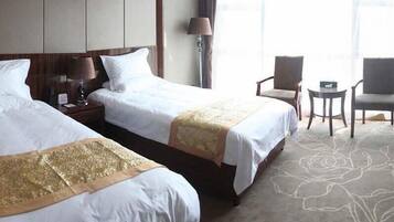 A hotel room with two beds, a desk, a chair, and a lamp.